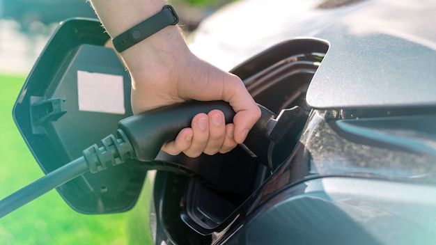 Hombre enchufando el cargador en un coche eléctrico en la estación de carga