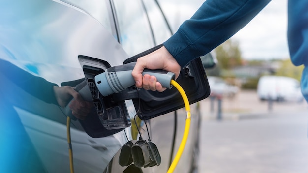 Hombre enchufando el cargador en un coche eléctrico en la estación de carga