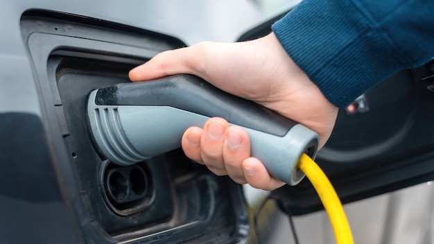 Hombre enchufando el cargador en un coche eléctrico en la estación de carga