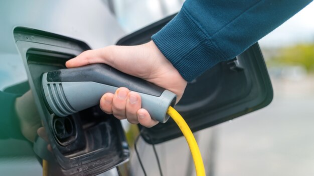 Hombre enchufando el cargador en un coche eléctrico en la estación de carga