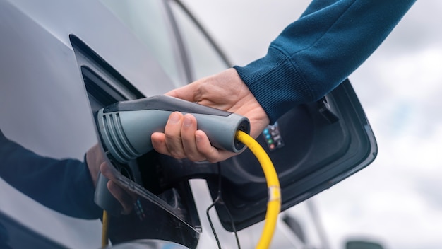 Hombre enchufando el cargador en un coche eléctrico en la estación de carga