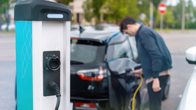 Hombre enchufando el cargador en un coche eléctrico en la estación de carga