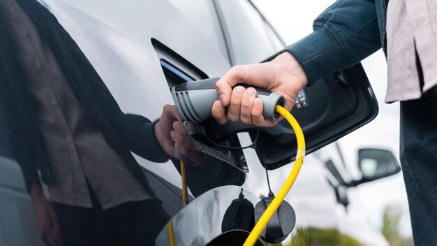 Hombre enchufando el cargador en un coche eléctrico en la estación de carga