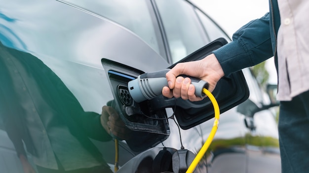 Hombre enchufando el cargador en un coche eléctrico en la estación de carga