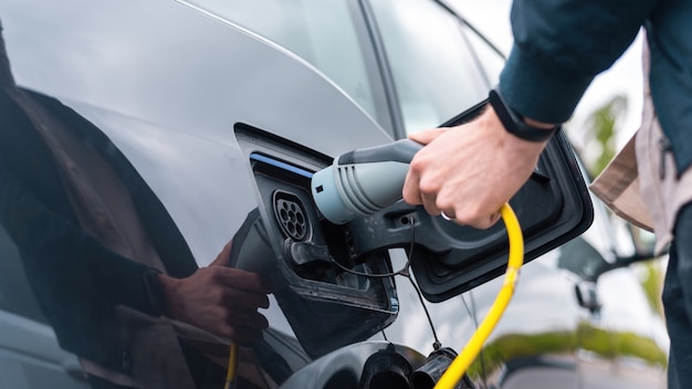 Hombre enchufando el cargador en un coche eléctrico en la estación de carga