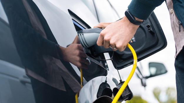 Hombre enchufando el cargador en un coche eléctrico en la estación de carga