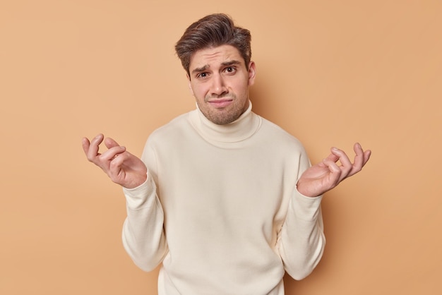 Foto gratuita el hombre se encoge de hombros se siente dubitativo caras difíciles elección viste cómodo cuello tortuga aislado en beige. no se que hacer en esta situacion