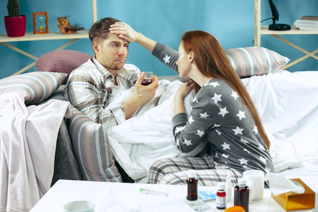 Hombre enfermo con fiebre acostado en la cama con temperatura. Su esposa lo cuida.