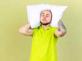 Foto gratuita hombre enfermo joven soñoliento sostiene la almohada detrás del cuello aislado en la pared verde oliva