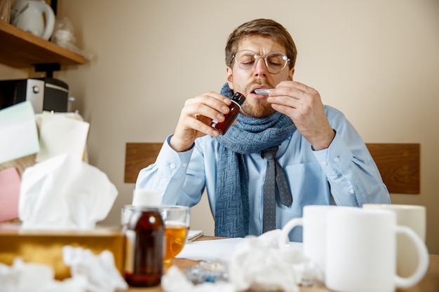 Foto gratuita hombre enfermo con mezcla medicinal trabajando en oficina, empresario resfriado, gripe estacional. gripe pandémica, prevención de enfermedades, enfermedad, virus, infección, temperatura, fiebre y concepto de gripe