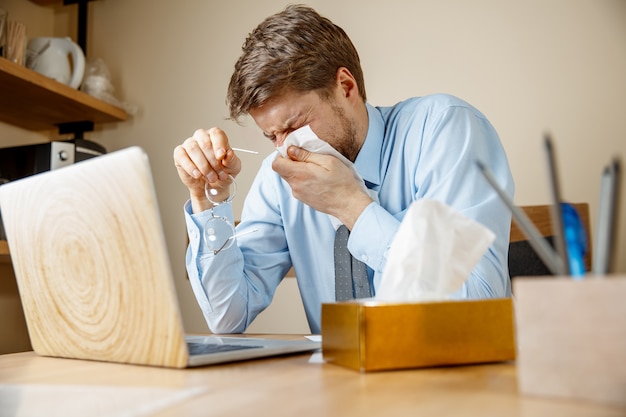 Hombre enfermo con pañuelo estornudando sonarse la nariz mientras trabajaba en la oficina, el empresario se resfrió, gripe estacional.