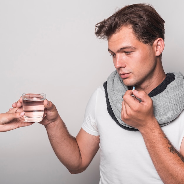 Hombre enfermo que sostiene el vaso de agua de la mano de la persona que toma la cápsula