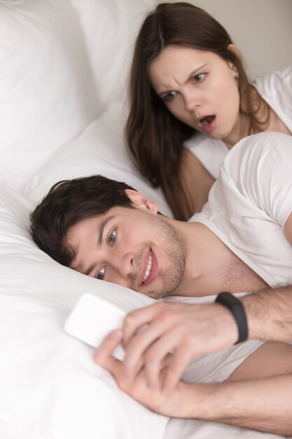 Hombre engañando usando el teléfono móvil en la cama, novia atrapándolo