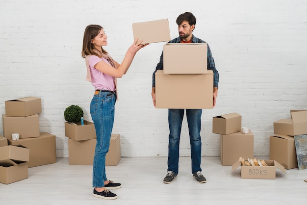 Hombre enojado mirando a su esposa apilando las cajas de cartón sobre sus manos