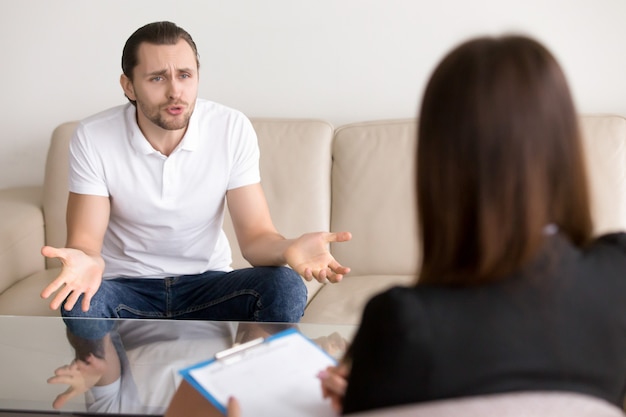 Foto gratuita hombre enojado con problemas que se queja a la psicoterapeuta femenina, hablando de problemas