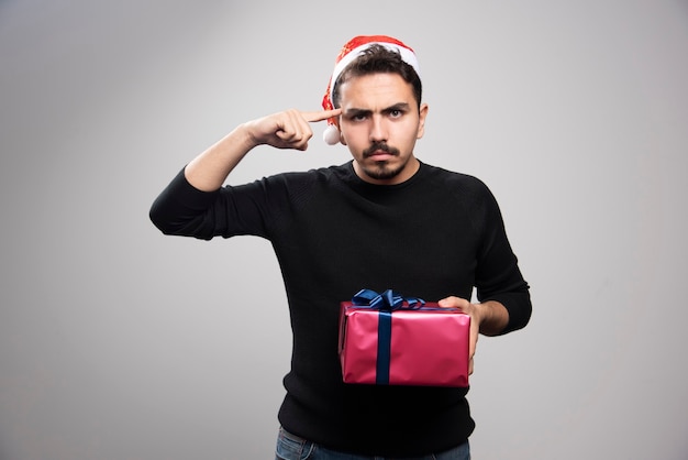 Hombre enojado sosteniendo una caja de regalo sobre una pared gris.