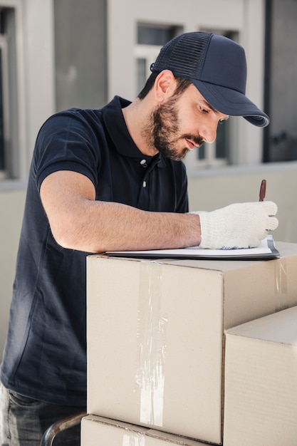 Hombre de entrega escribiendo en portapapeles sobre cajas de cartón apiladas