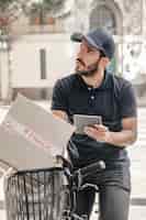Foto gratuita hombre de entrega sentado en bicicleta con tableta digital y paquete