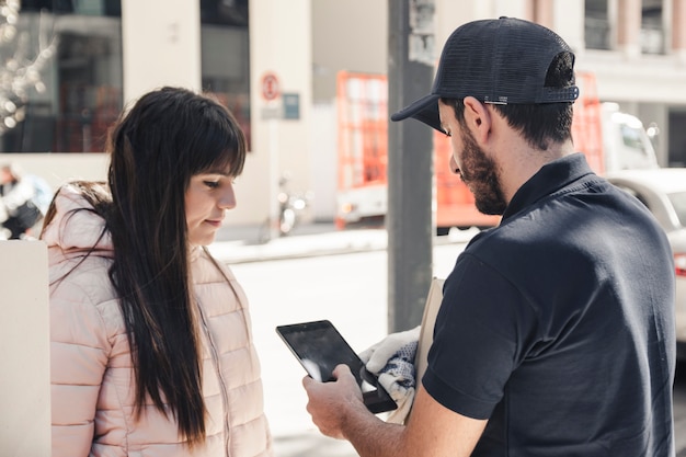 Hombre de entrega con tableta digital cerca de cliente femenino