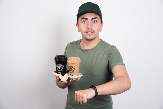 Hombre de entrega con tazas de café para llevar sobre fondo blanco.