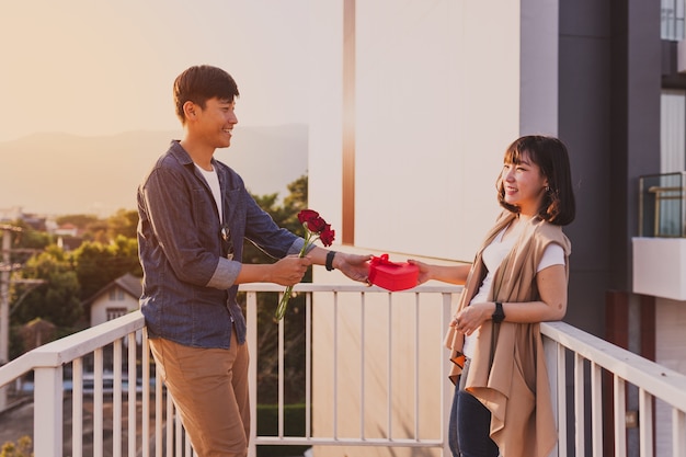 Hombre entregando a su novia una caja con forma de corazón y una rosa