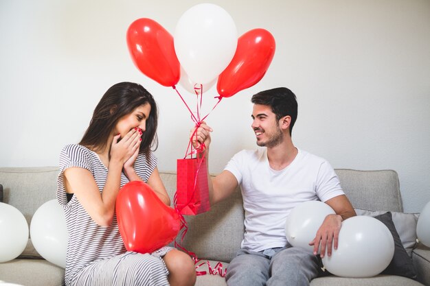 Hombre entregando a su novia globos y una bolsa roja