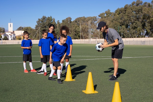 Hombre entrenando a niños jugando al fútbol tiro completo