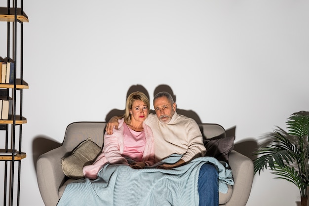 Hombre envejecido abrazando a la mujer y viendo la televisión en el sofá