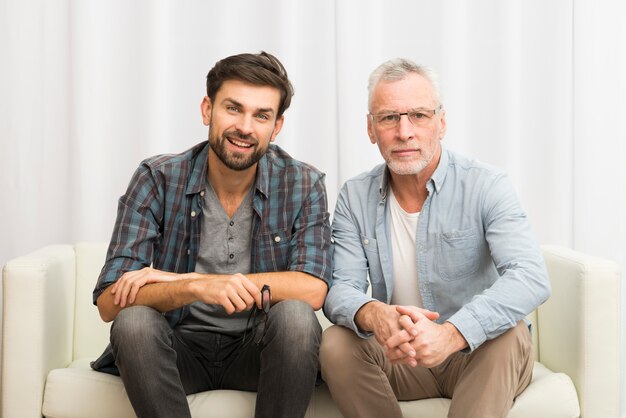 Hombre envejecido y chico feliz joven en sofá