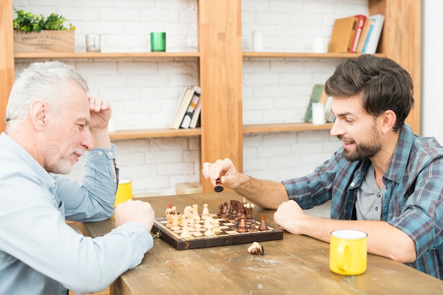 Hombre envejecido y chico joven jugando al ajedrez en la mesa en la habitación