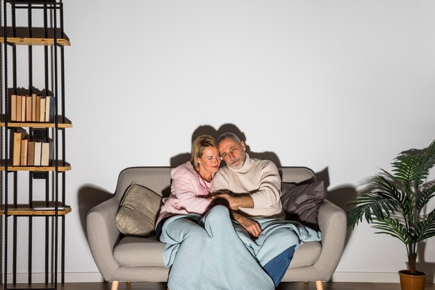 Hombre envejecido cogidos de la mano con la mujer y viendo la televisión en el sofá