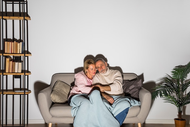 Hombre envejecido cogidos de la mano con la mujer y viendo la televisión en el sofá