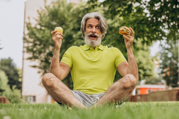 Hombre envejecido eligiendo entre hamburguesa y manzana