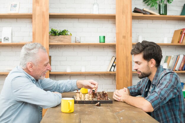 Hombre envejecido feliz y chico joven jugando al ajedrez en la mesa en la habitación