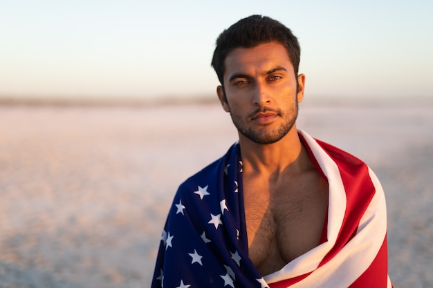 Hombre envuelto en la bandera americana de pie en la playa