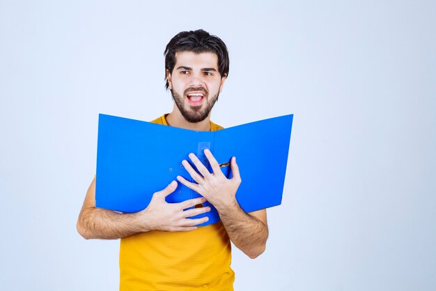 Hombre escondiendo su rostro detrás de una carpeta azul.