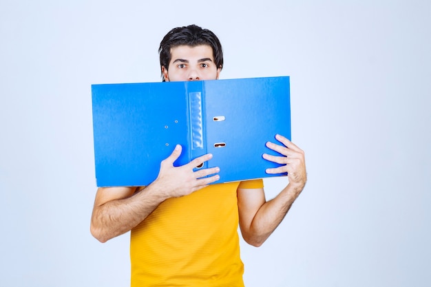 Hombre escondiendo su rostro detrás de una carpeta azul.