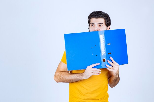 Hombre escondiendo su rostro detrás de una carpeta azul.