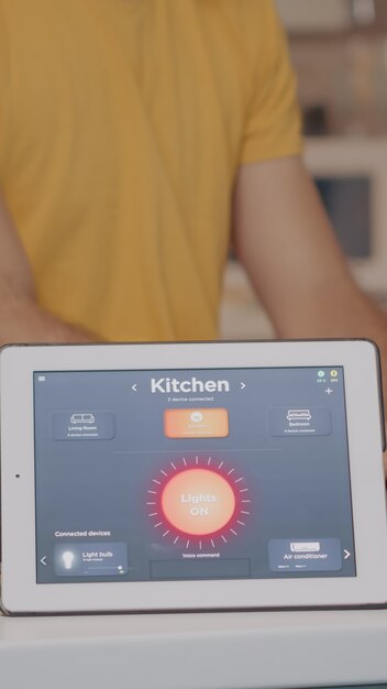 Hombre escribiendo en una computadora portátil que trabaja desde casa con un sistema de iluminación de automatización mediante una aplicación controlada por voz en la tableta que enciende la luz