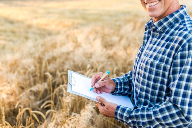 Hombre escribiendo en un portapapeles en un campo de trigo