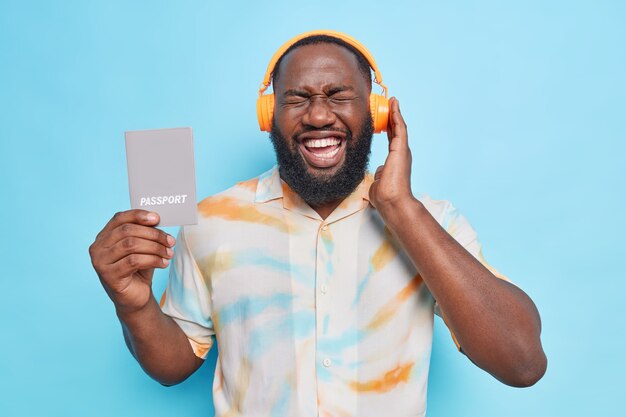 El hombre escucha música a través de auriculares inalámbricos se ríe positivamente sostiene el pasaporte que va a viajar