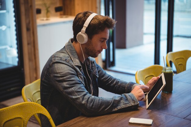 Hombre escuchando música con auriculares mientras usa tableta digital