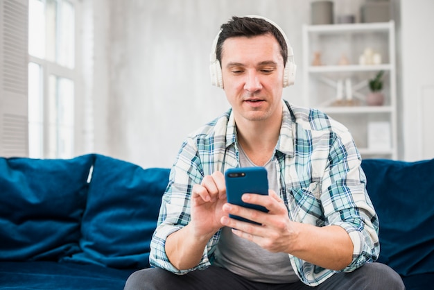 Foto gratuita hombre escuchando música en auriculares y usando un teléfono inteligente en el sofá