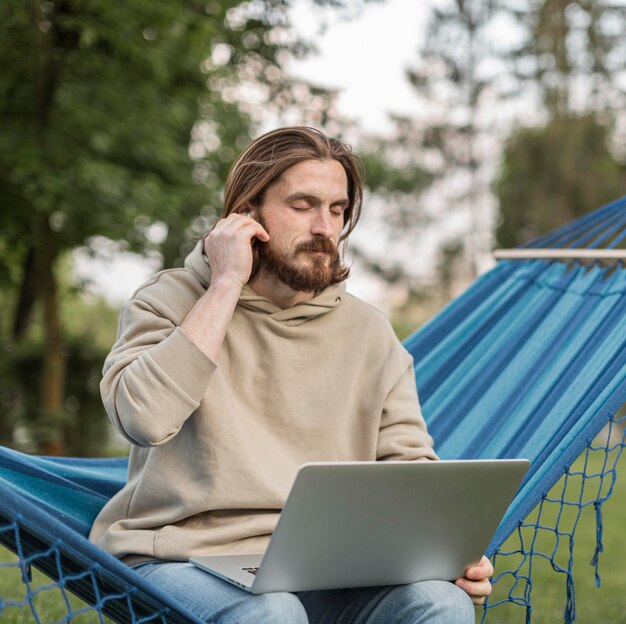 Hombre escuchando música en hamaca con laptop