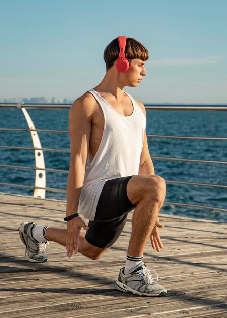 Hombre escuchando música en la playa con auriculares mientras hace ejercicio