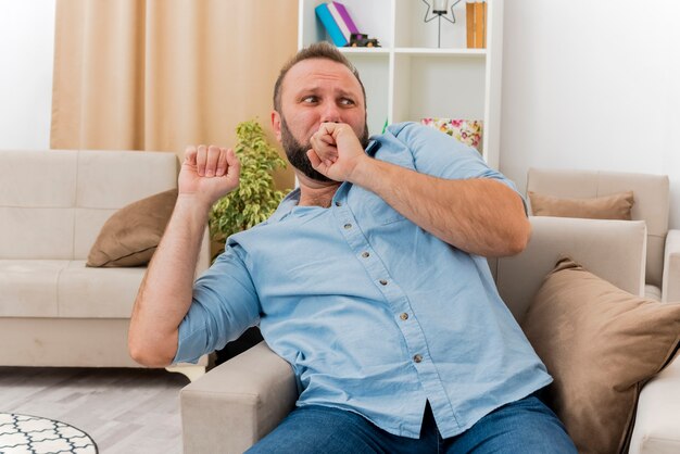 Hombre eslavo adulto asustado se sienta en un sillón mirando al lado dentro de la sala de estar