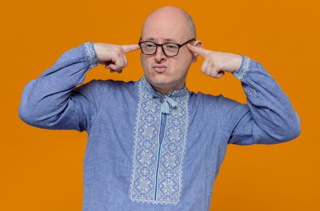 Hombre eslavo adulto confiado en camisa azul y con gafas ópticas poniendo los dedos en las sienes y mirando de lado