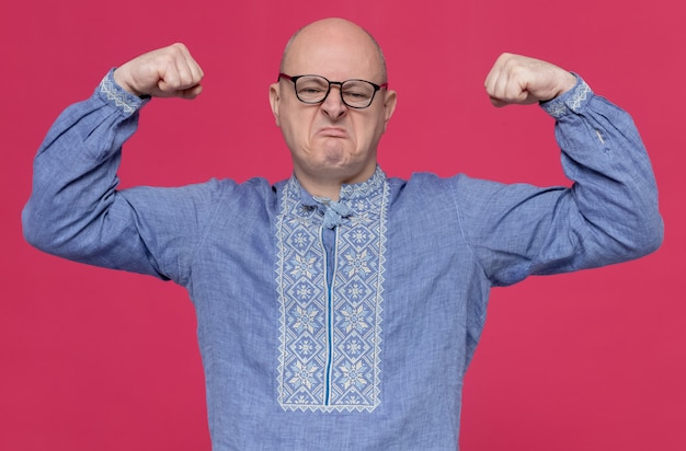 Foto gratuita hombre eslavo adulto confiado en camisa azul con gafas ópticas tensando sus bíceps