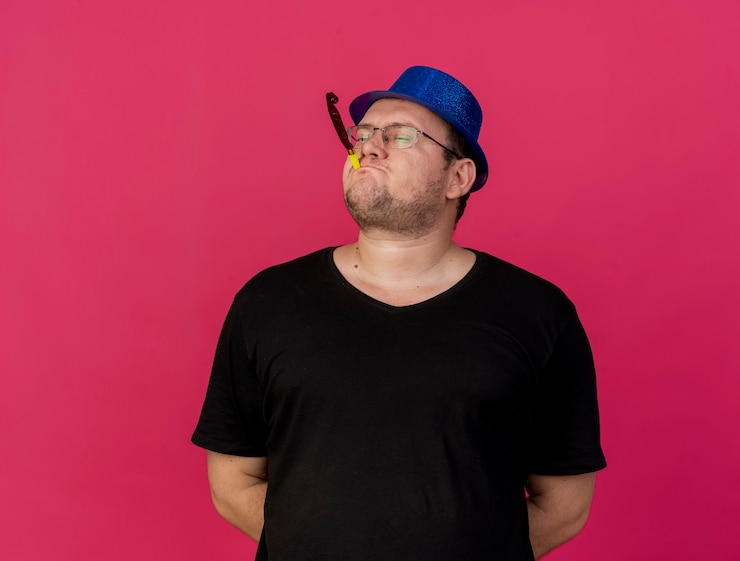Foto gratuito hombre eslavo adulto confiado en gafas ópticas con sombrero de fiesta azul soplando silbato de fiesta