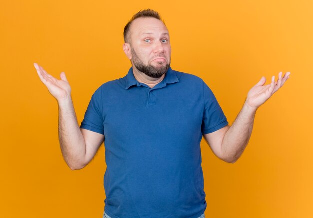 Hombre eslavo adulto confundido mostrando las manos vacías aisladas en la pared naranja